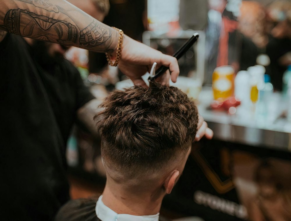 A barber finishing a short textured haircut in a bright room